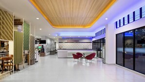 Un moderno vestíbulo de hotel con un mostrador de recepción, sillas rojas y un amplio ventanal con vistas al exterior.