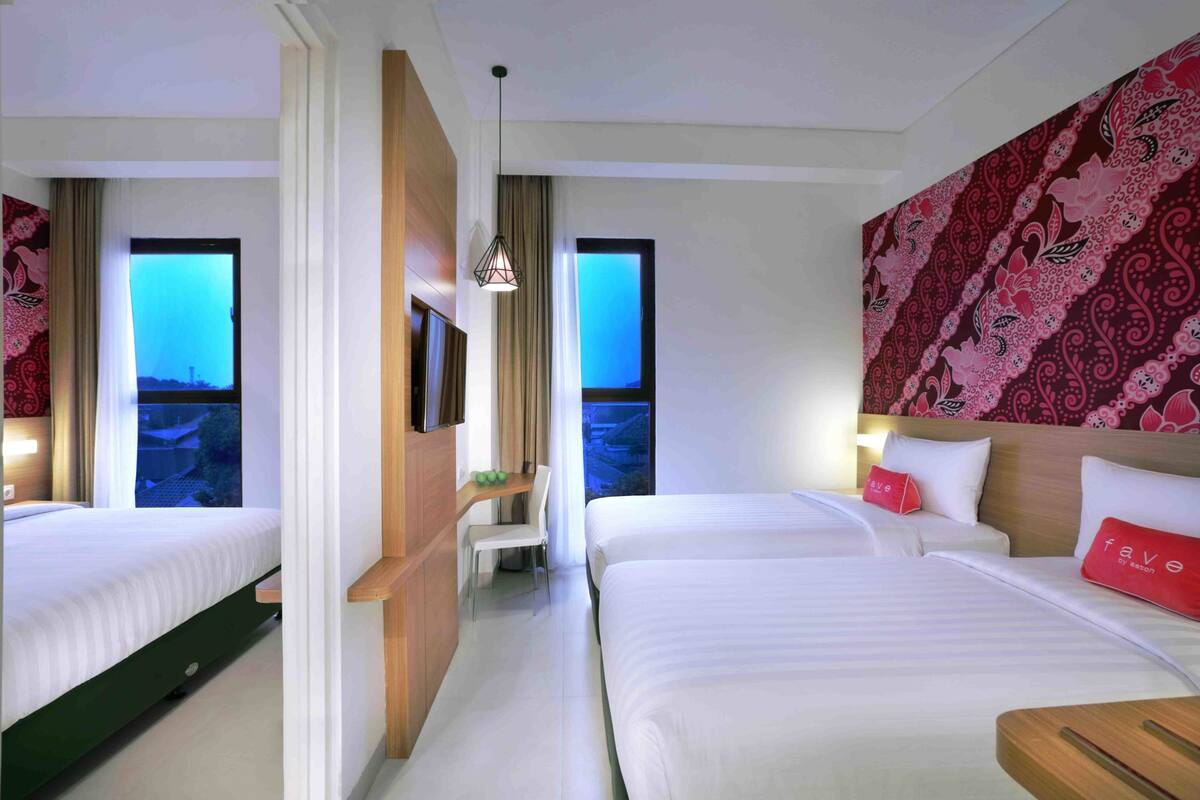 A hotel room with two beds, a desk, and a view of the cityscape.