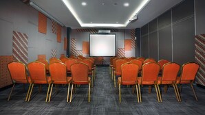 Un salón de conferencias con hileras de sillas color naranja, una pantalla grande y paredes con diseños.