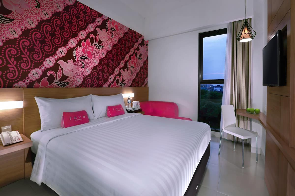 A modern hotel room with a large bed, a flat-screen TV, a bedside table with a phone, and a view of the city through the window.