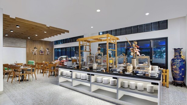 Un comedor moderno de hotel con una barra de buffet, techo de madera y ventanas grandes.