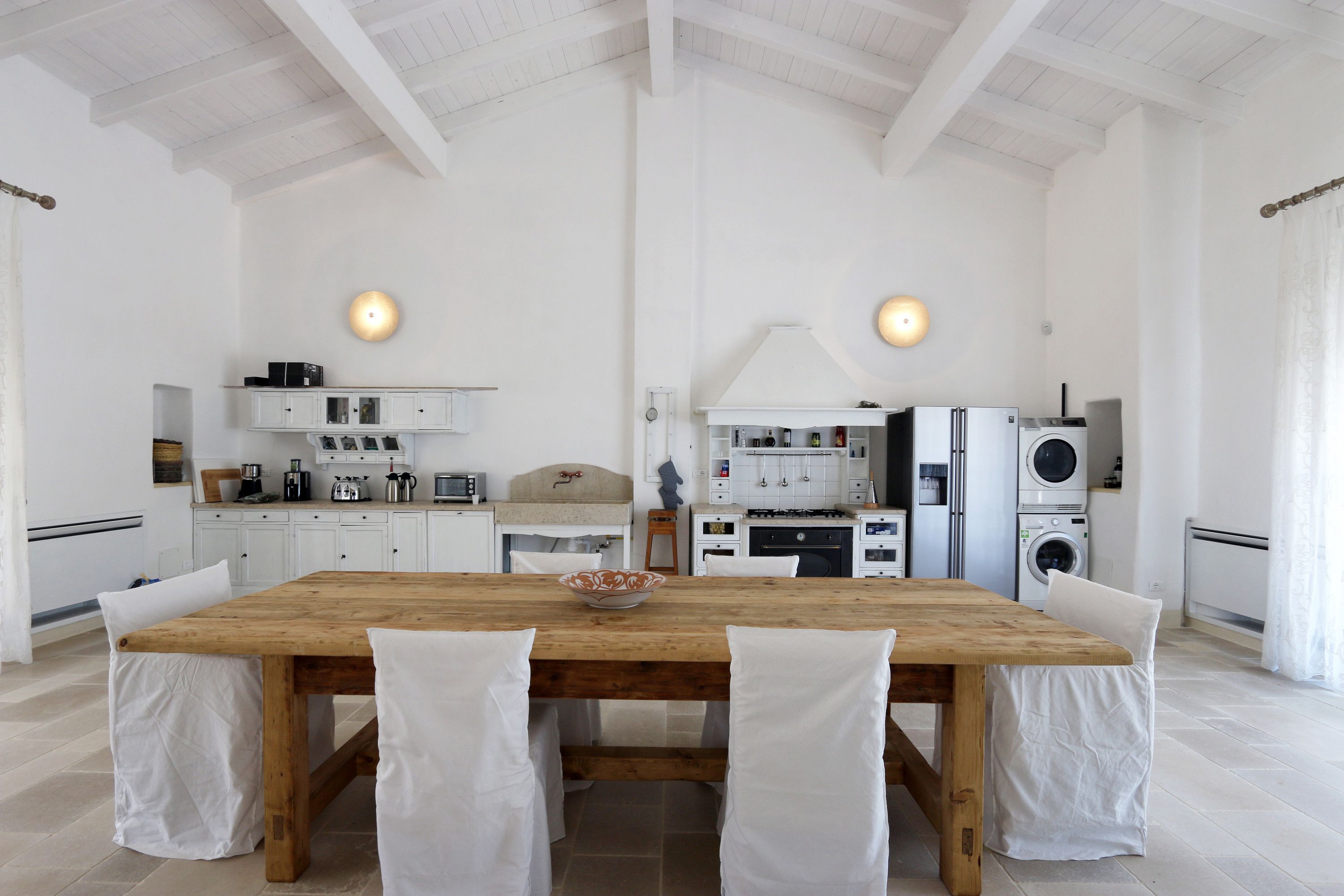 A spacious kitchen with white cabinetry, a wooden dining table, and two pendant lights.