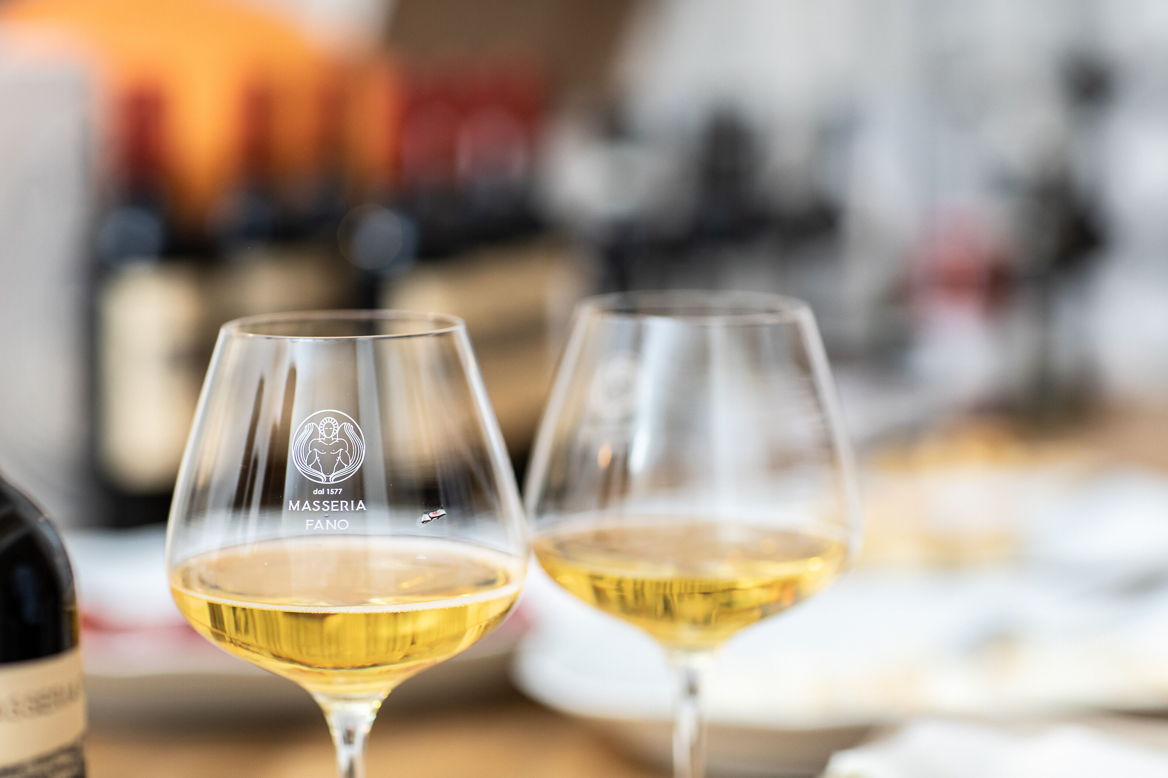 Deux verres à vin sont posés sur une table, avec un arrière-plan flou composé de bouteilles.
