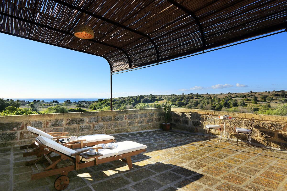 Una terraza con sillones de descanso y una mesa, con vistas a un paisaje pintoresco.