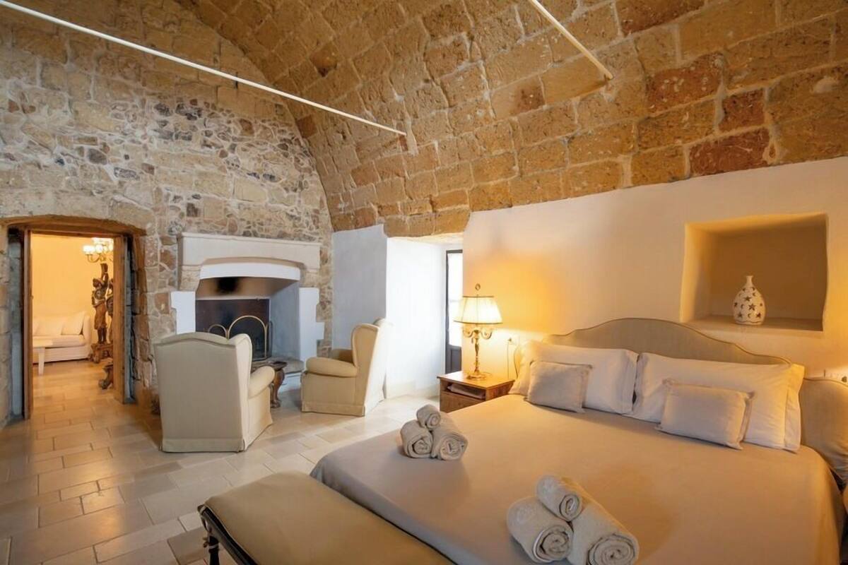 Un dormitorio acogedor con pared de piedra, chimenea, cama con toallas enrolladas y mesita de noche con lámpara.