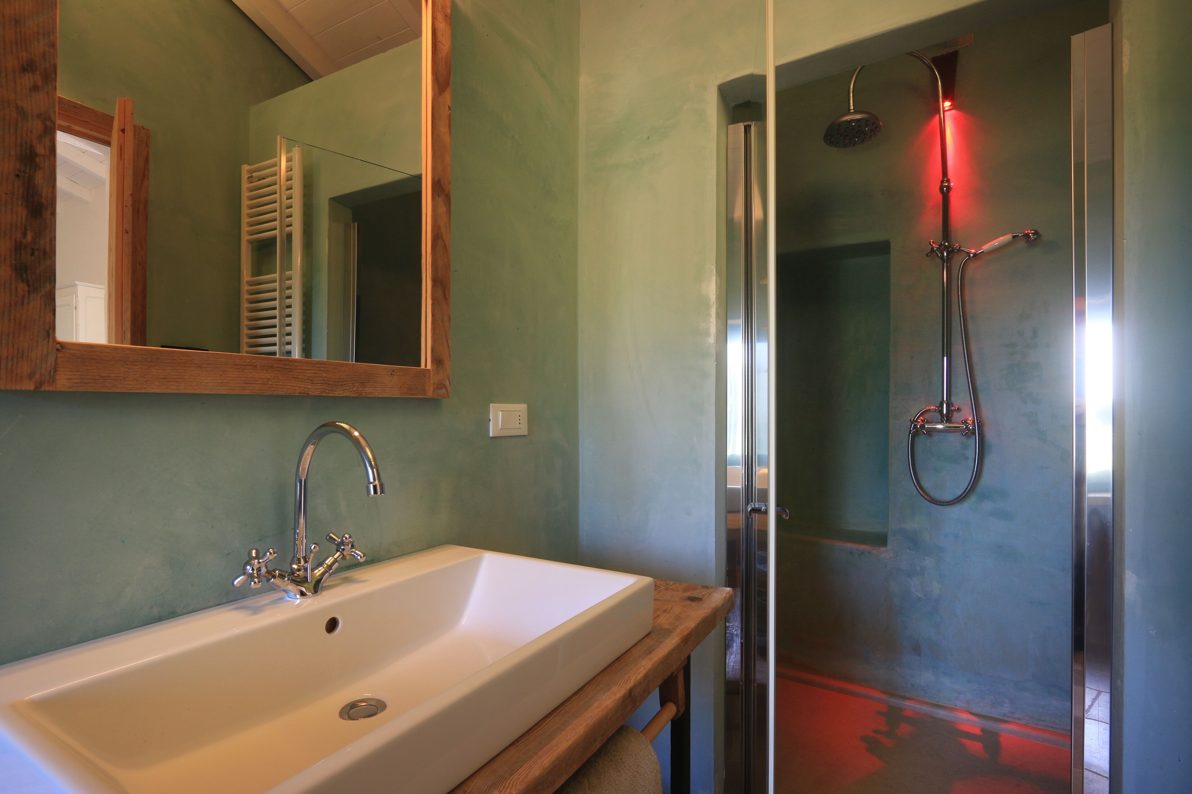 A bathroom with a white sink, a mirror, and a shower with a red light.