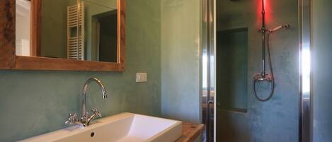 A bathroom with a white sink, a mirror, and a shower with a red light.