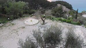 A landscaped garden with stone pathways, trees, and a view of the sea at sunset. - La Casa D' Irene (Lefkada)
