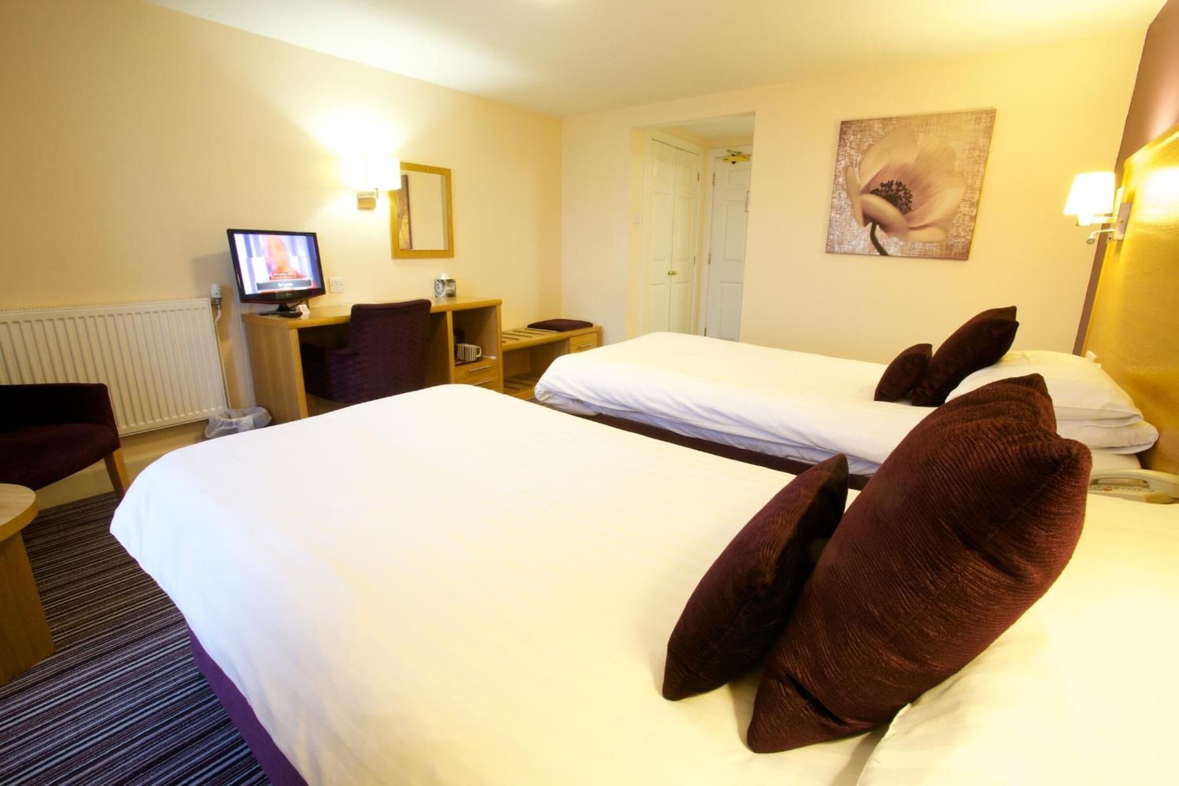 Una habitación de hotel con dos camas, un escritorio con computadora, una silla y un cuadro en la pared.