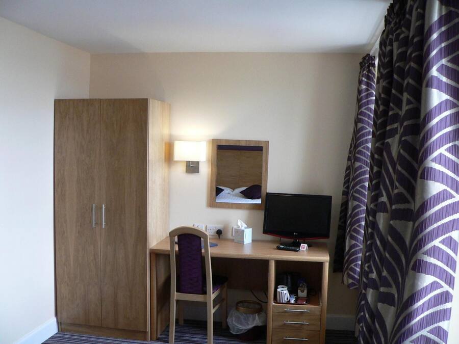 A hotel room with a wooden desk, a computer, a chair, a bed, and a wardrobe.