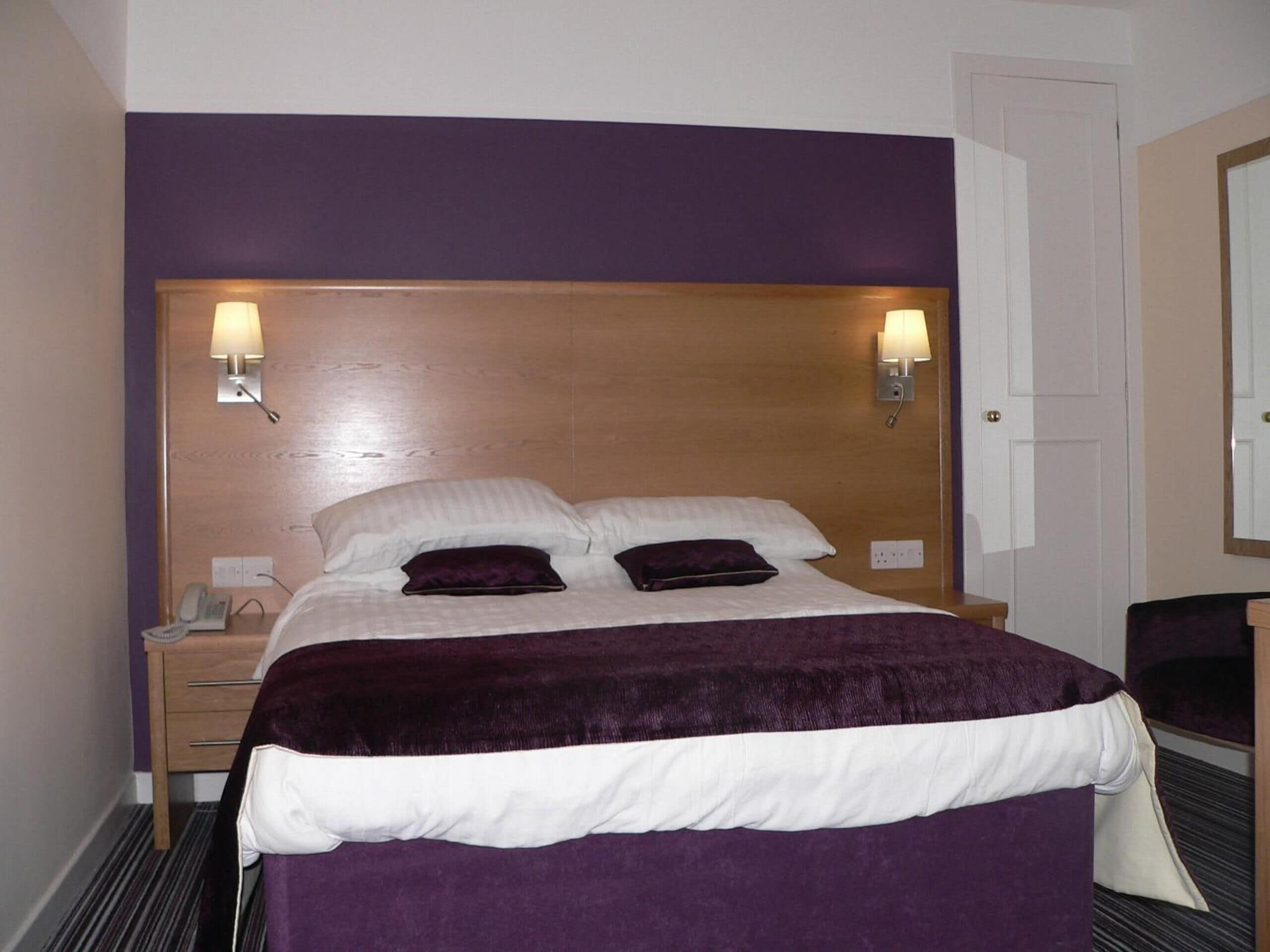 A hotel room with a bed, two bedside lamps, a nightstand, a telephone, and a mirror.