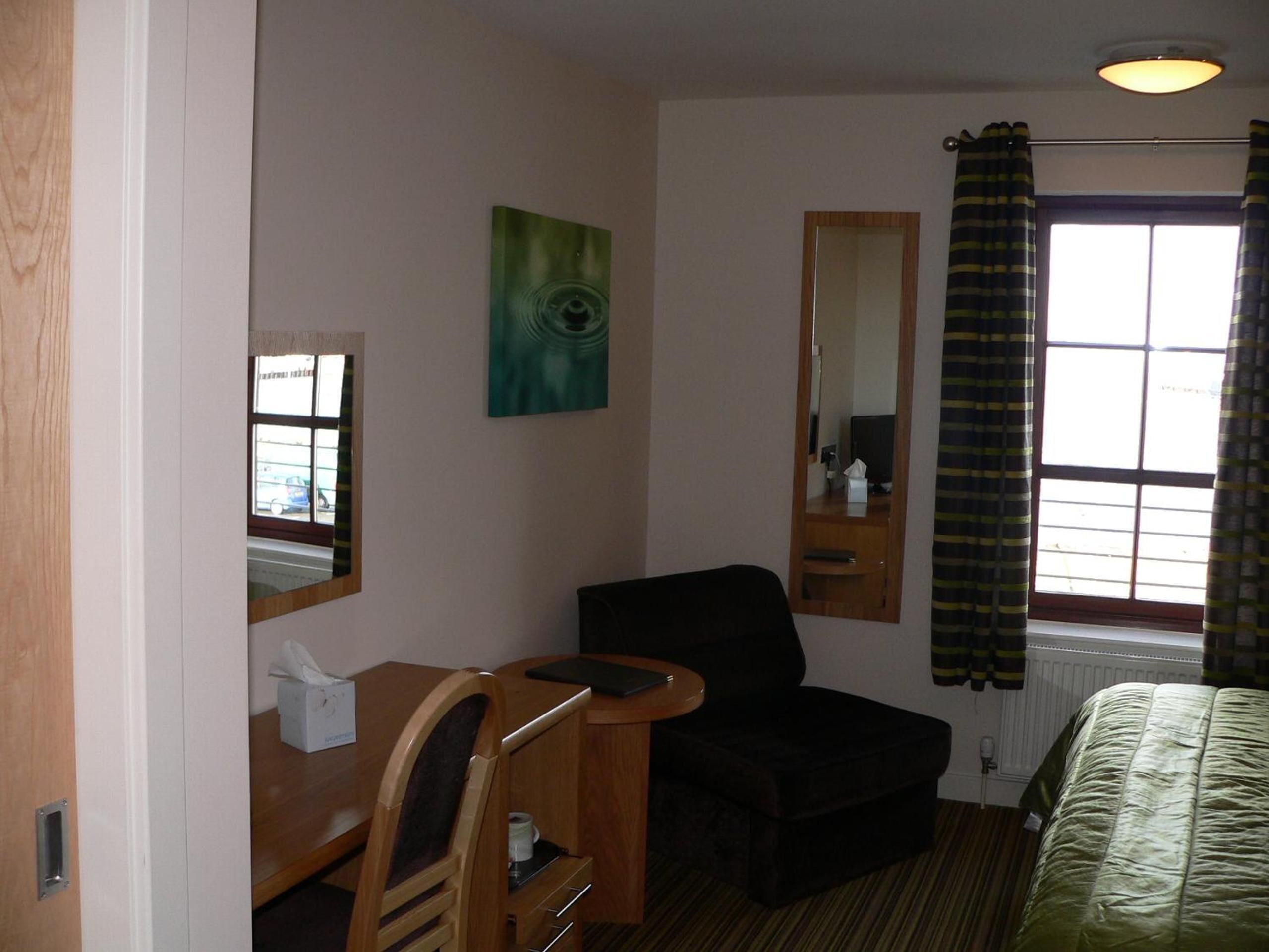 Habitación de hotel con escritorio, silla, cama y ventana con cortinas.