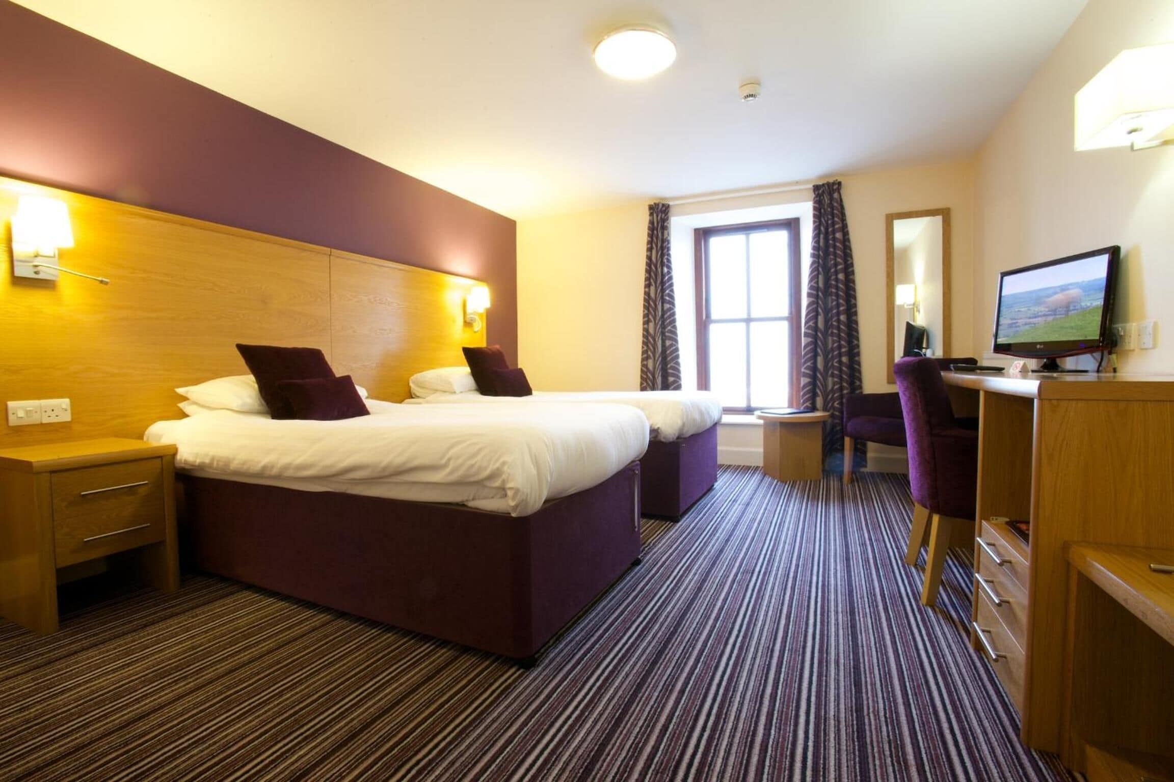 A hotel room with two beds, a desk with a computer, a chair, and a TV.