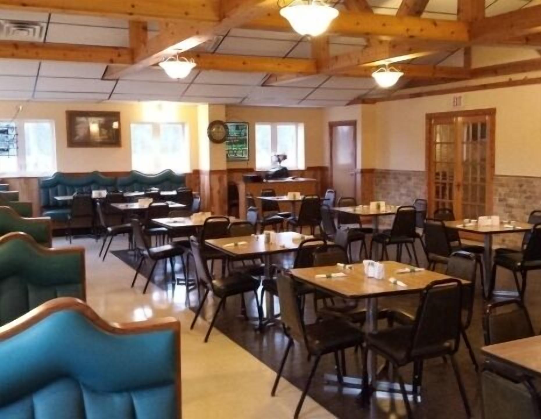 Un restaurant avec des banquettes et des tables, des poutres en bois au plafond et une horloge au mur.
