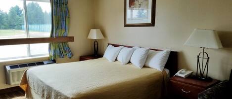 A hotel room with a large bed, two bedside tables, a window with curtains, a framed picture on the wall, and a telephone on one of the tables.