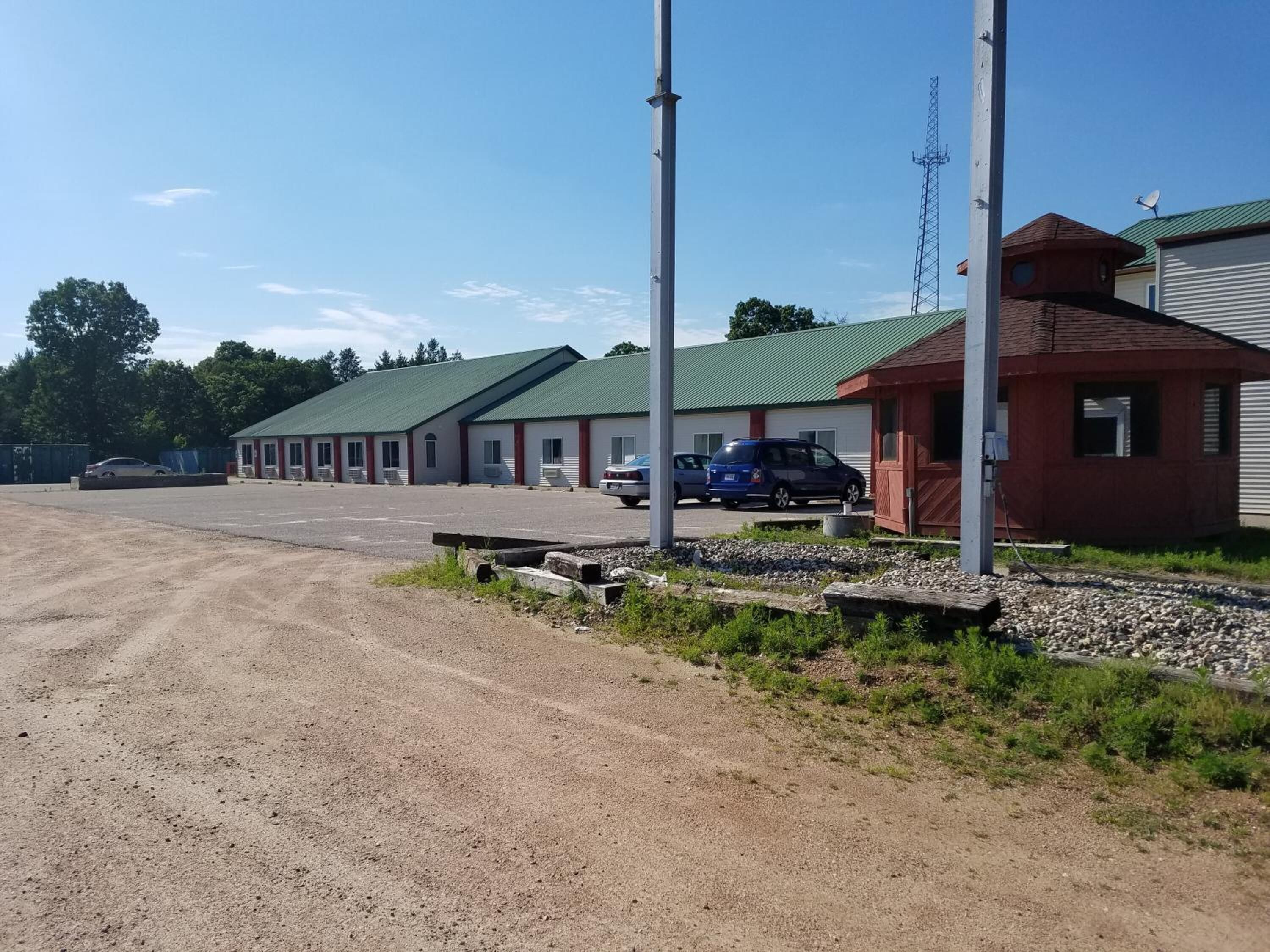 Um motel com várias salas, estacionamento e um pequeno edifício vermelho.