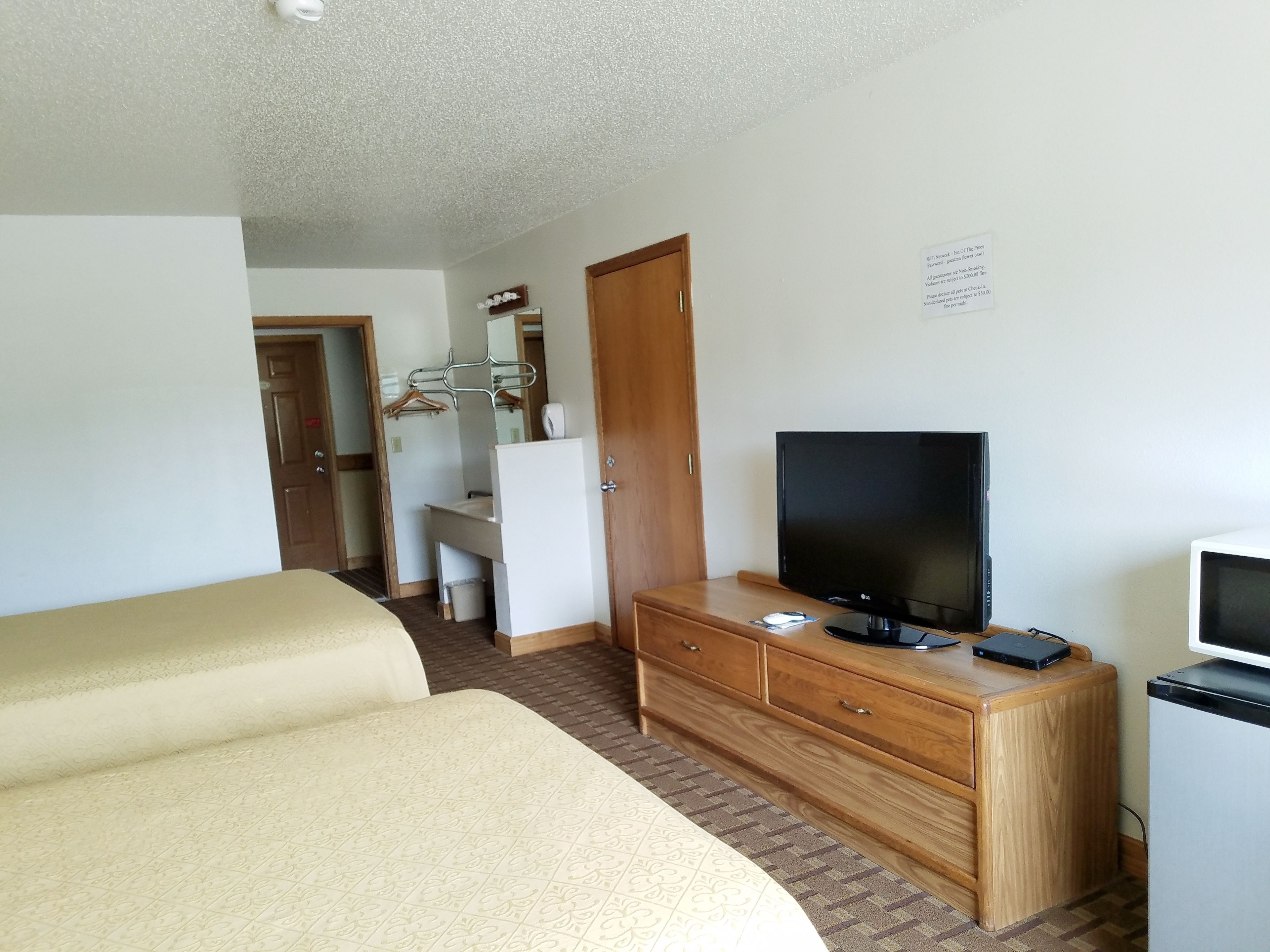 Une chambre d’hôtel avec un lit, une télévision, une commode en bois et une salle de bain visible à travers une porte ouverte.