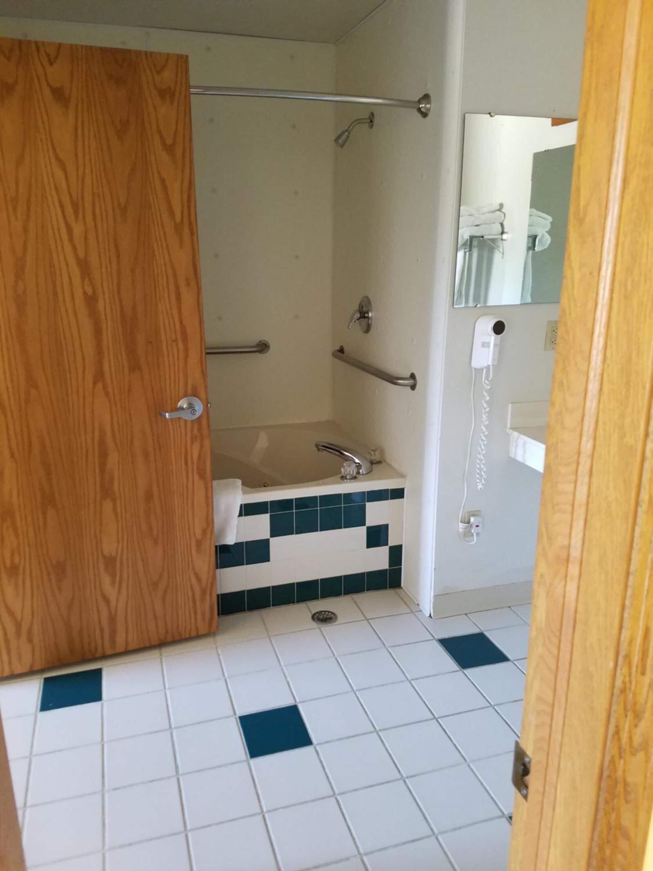 Un baño con puerta de madera, ducha con barras de apoyo, lavamanos y espejo.