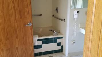 Un baño con puerta de madera, ducha con barras de apoyo, lavamanos y espejo.