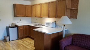 A compact kitchen with wooden cabinets, a microwave, a sink, and a small refrigerator.