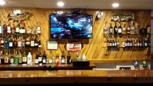 A bar area with a television mounted on the wall, shelves of liquor bottles, and a wooden floor.