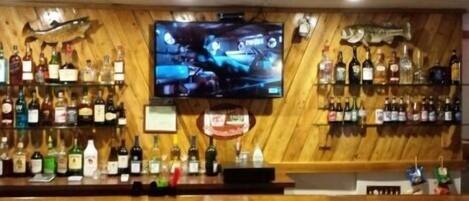 Eine Bar mit einem an der Wand befestigten Fernseher, Regalen voller Spirituosen und einem Holzboden.