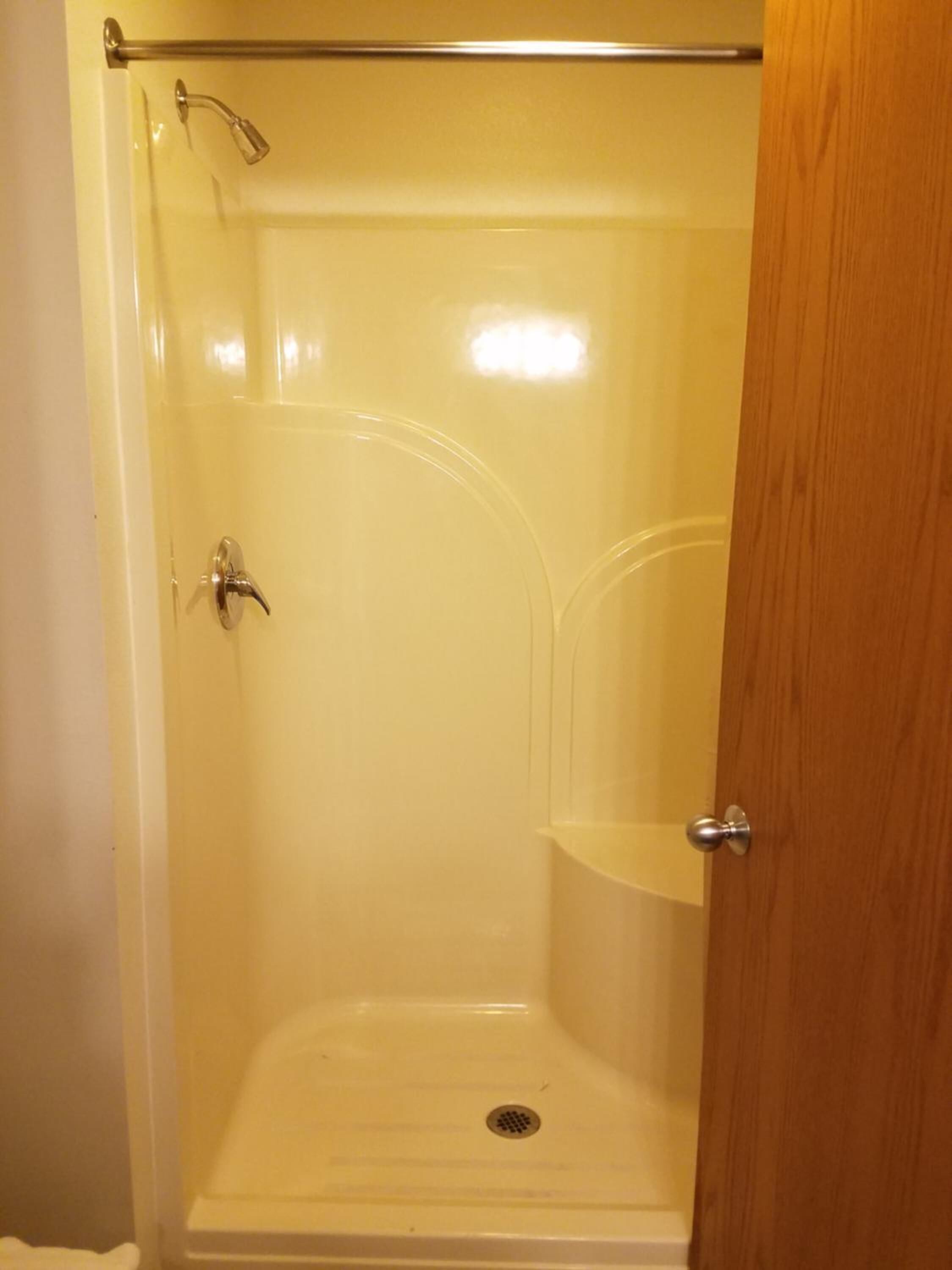 A glass-enclosed shower stall with a showerhead and a handheld shower attachment.
