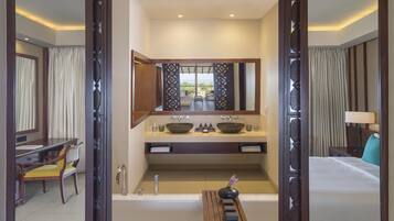 A hotel room with a large mirror, a bathtub, a vanity with a bowl sink, a desk with a chair, and a bed.