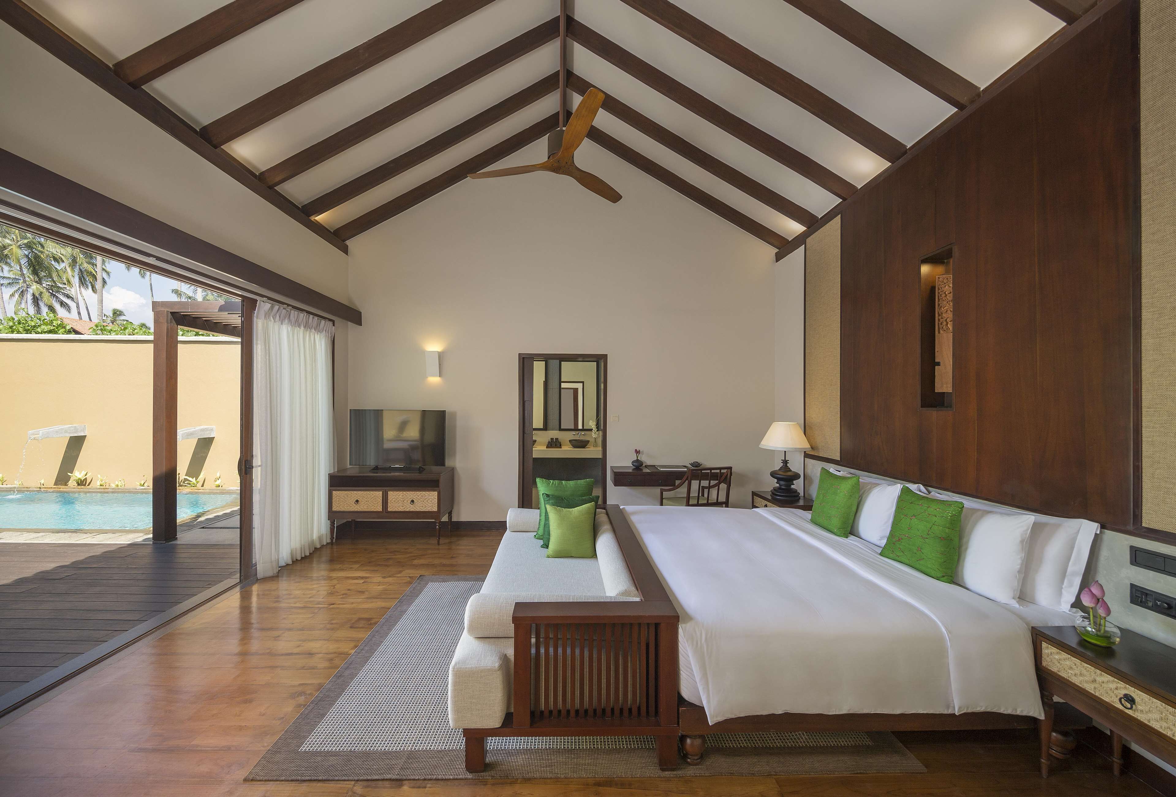 A spacious bedroom with a large bed, wooden headboard, and a view of a swimming pool.