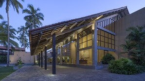 A modern hotel with a covered walkway, large windows, and palm trees. - Anantara Kalutara Resort (Kalutara)