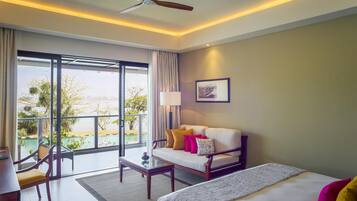 A hotel room with a bed, a sofa, a coffee table, a desk, and a view of a pool and greenery.