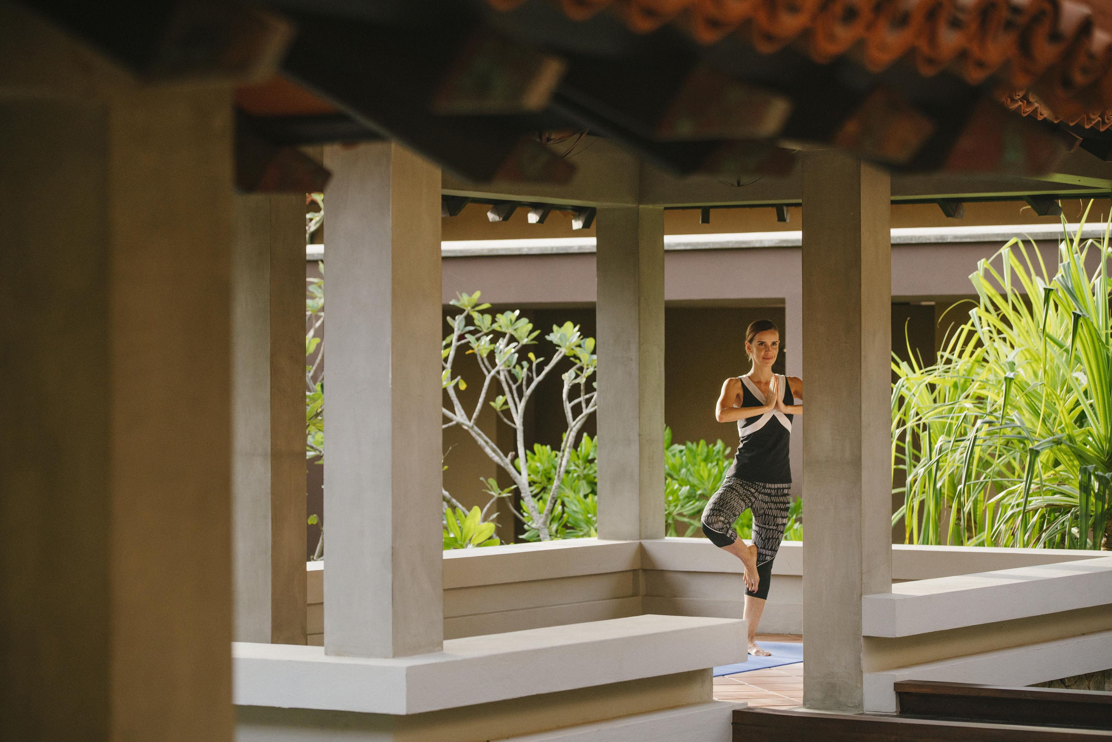 A person exercising on a wooden deck with a pergola overhead, surrounded by greenery.