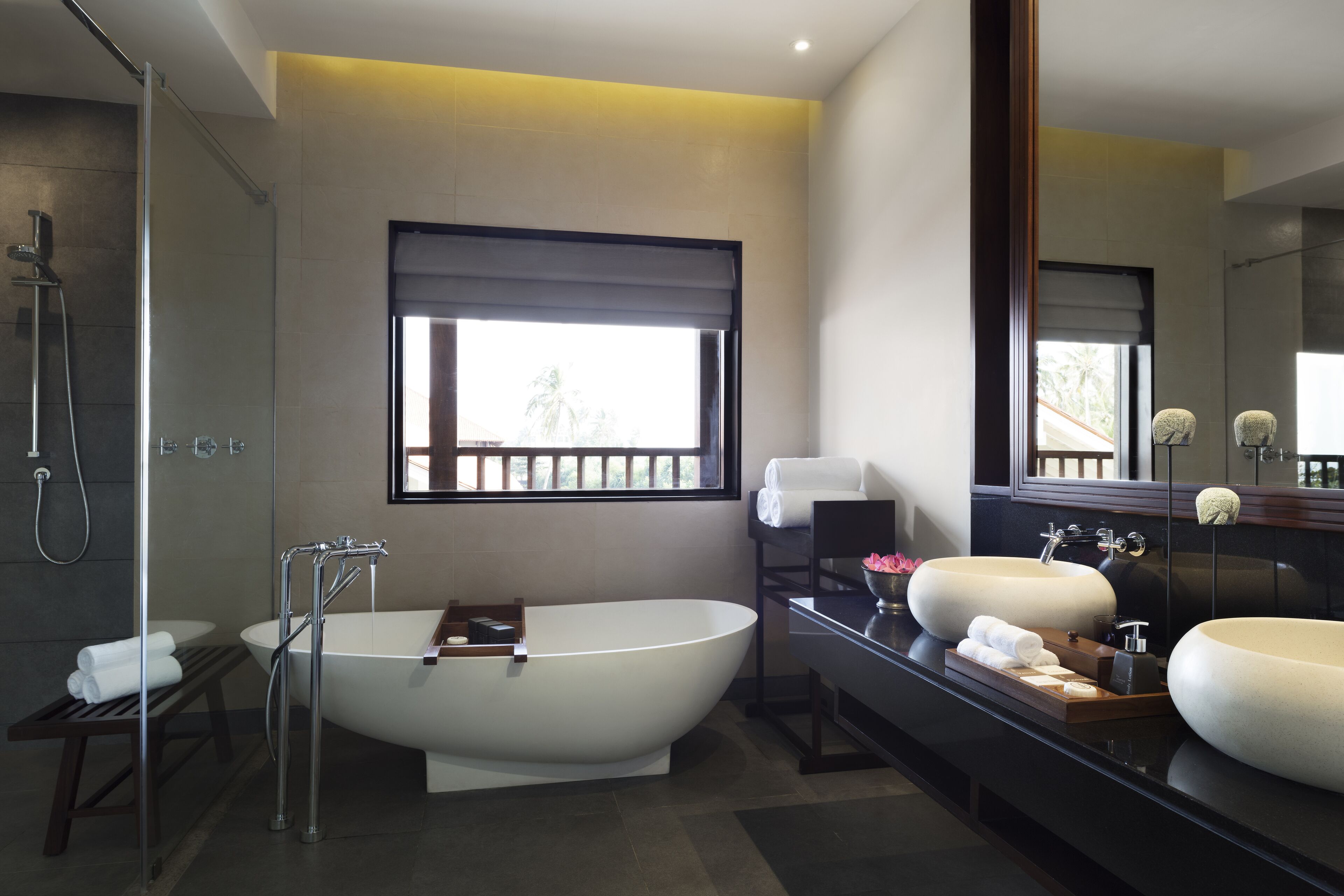 A modern bathroom with a freestanding bathtub, two sinks, a large mirror, and a window with a view.