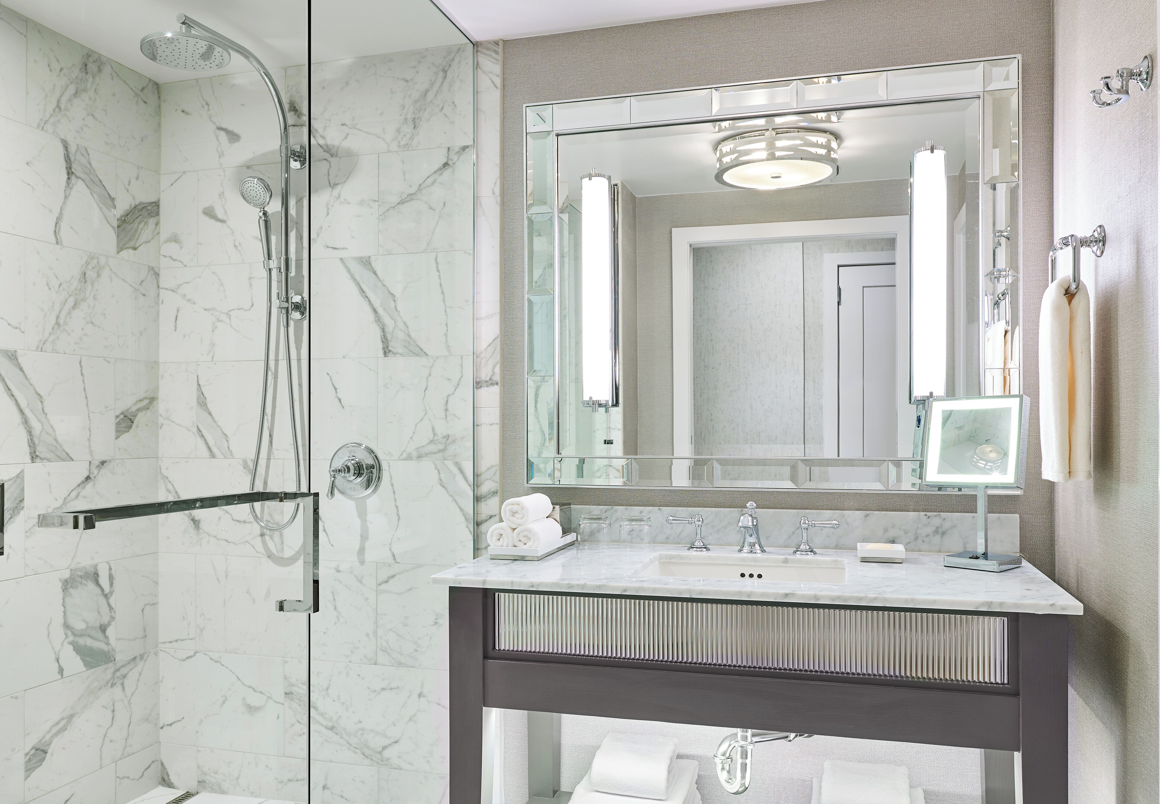 A modern bathroom with a glass-enclosed shower, a large mirror, and a marble-tiled wall.