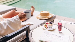 A poolside view with a person relaxing, a drink, a hat, and a newspaper titled "Vail Daily". - Grand Hyatt Vail Resort and Spa (Vail)