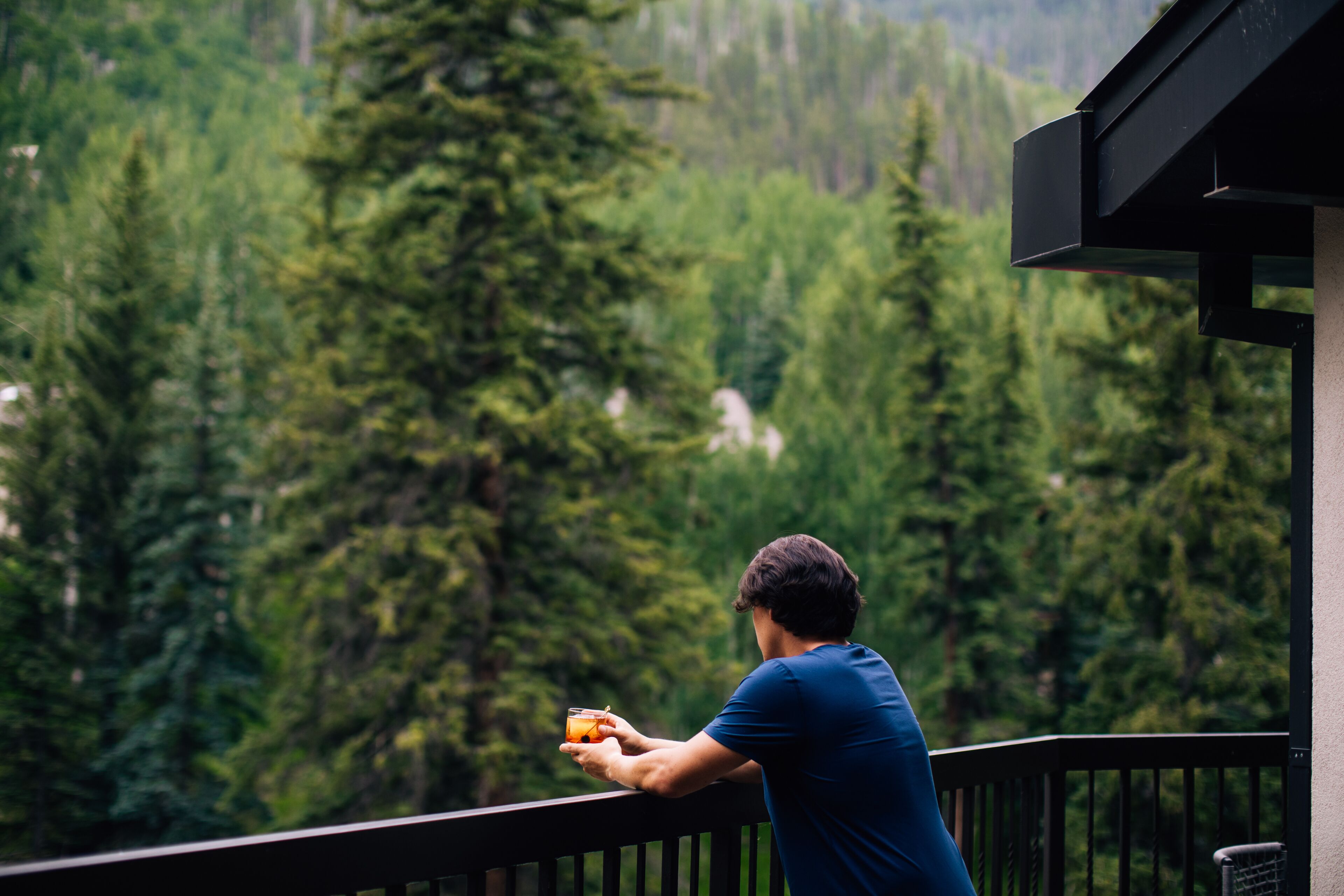 Ein Mann auf einem Balkon mit Blick auf ein bewaldetes Gebiet.