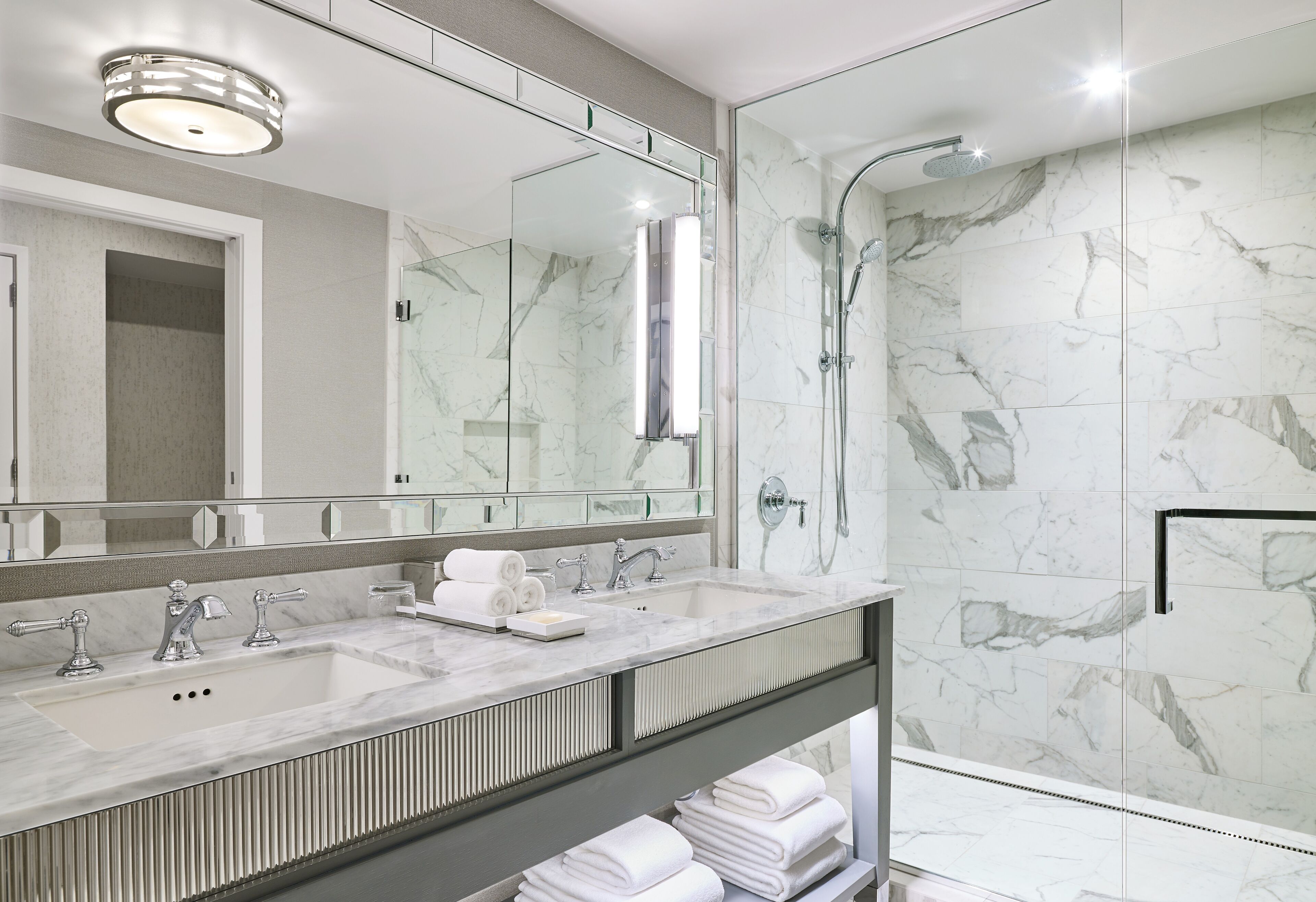Une salle de bain moderne avec un lavabo en marbre, un grand miroir et une douche à parois de verre.