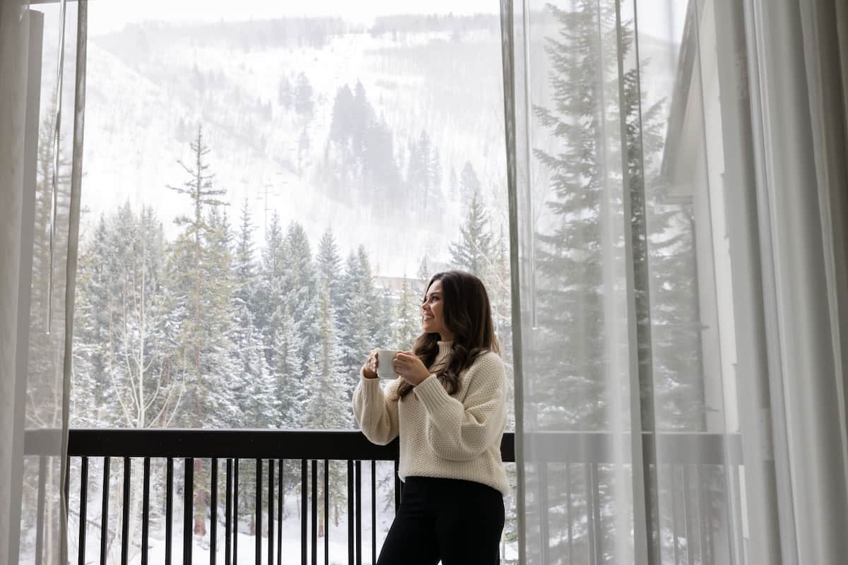Eine Person steht an einem Fenster mit Blick auf schneebedeckte Bäume.