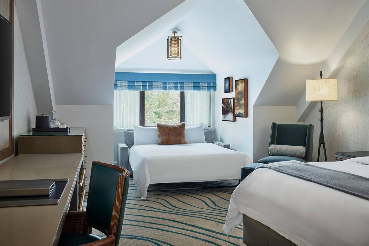 Ein Hotelzimmer mit einem großen Bett, einem Schreibtisch, einem Sessel und Blick ins Freie.