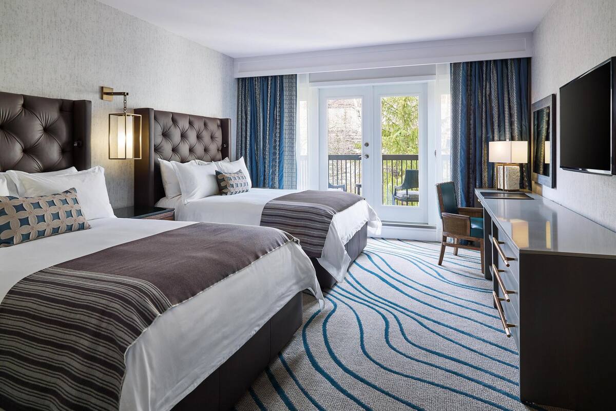 Ein Hotelzimmer mit zwei Betten, einem Schreibtisch, einem Fernseher und einem Balkon mit Vorhängen.