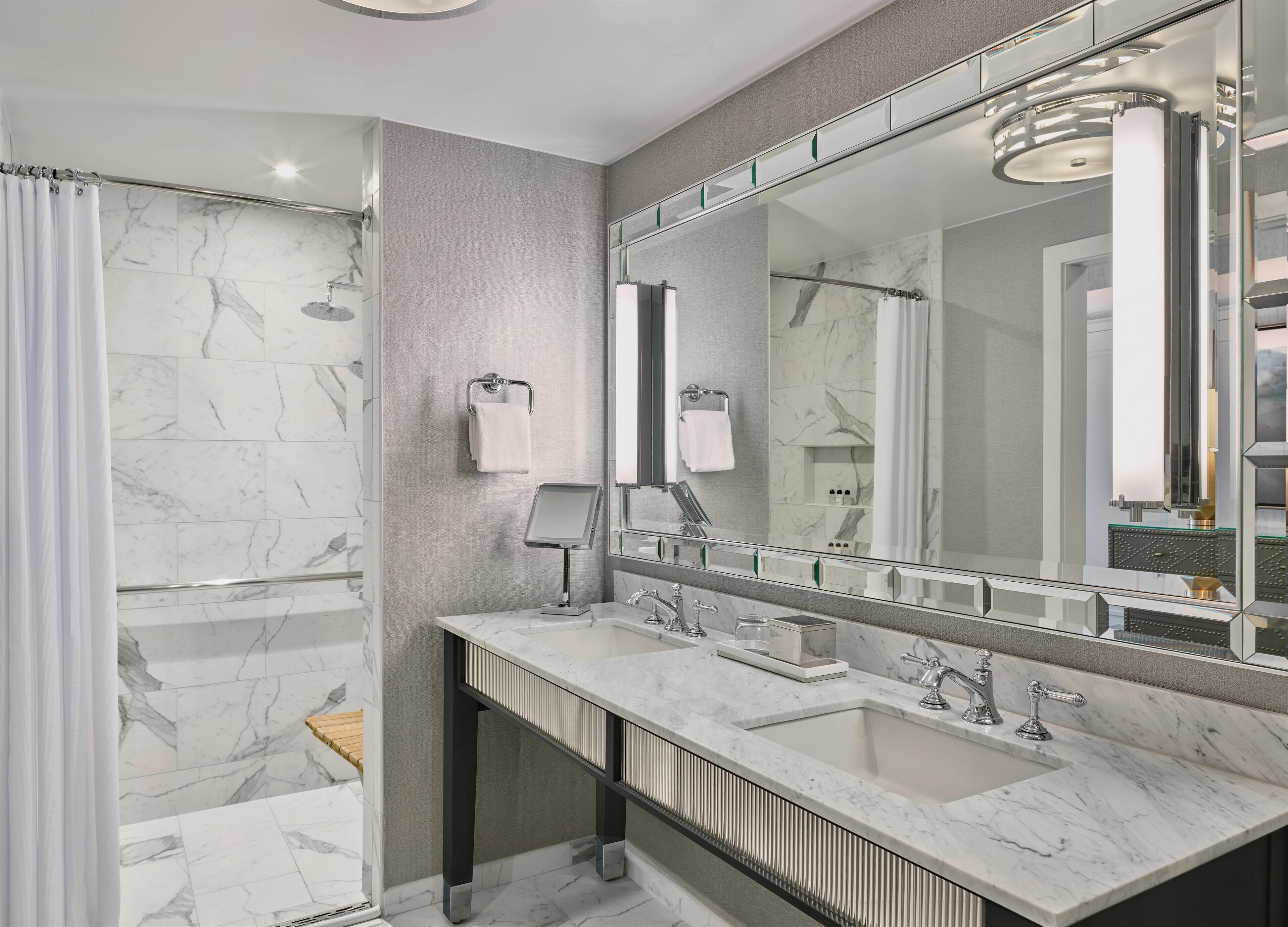Une salle de bain moderne avec une douche, deux lavabos, un grand miroir et un revêtement de sol en marbre.
