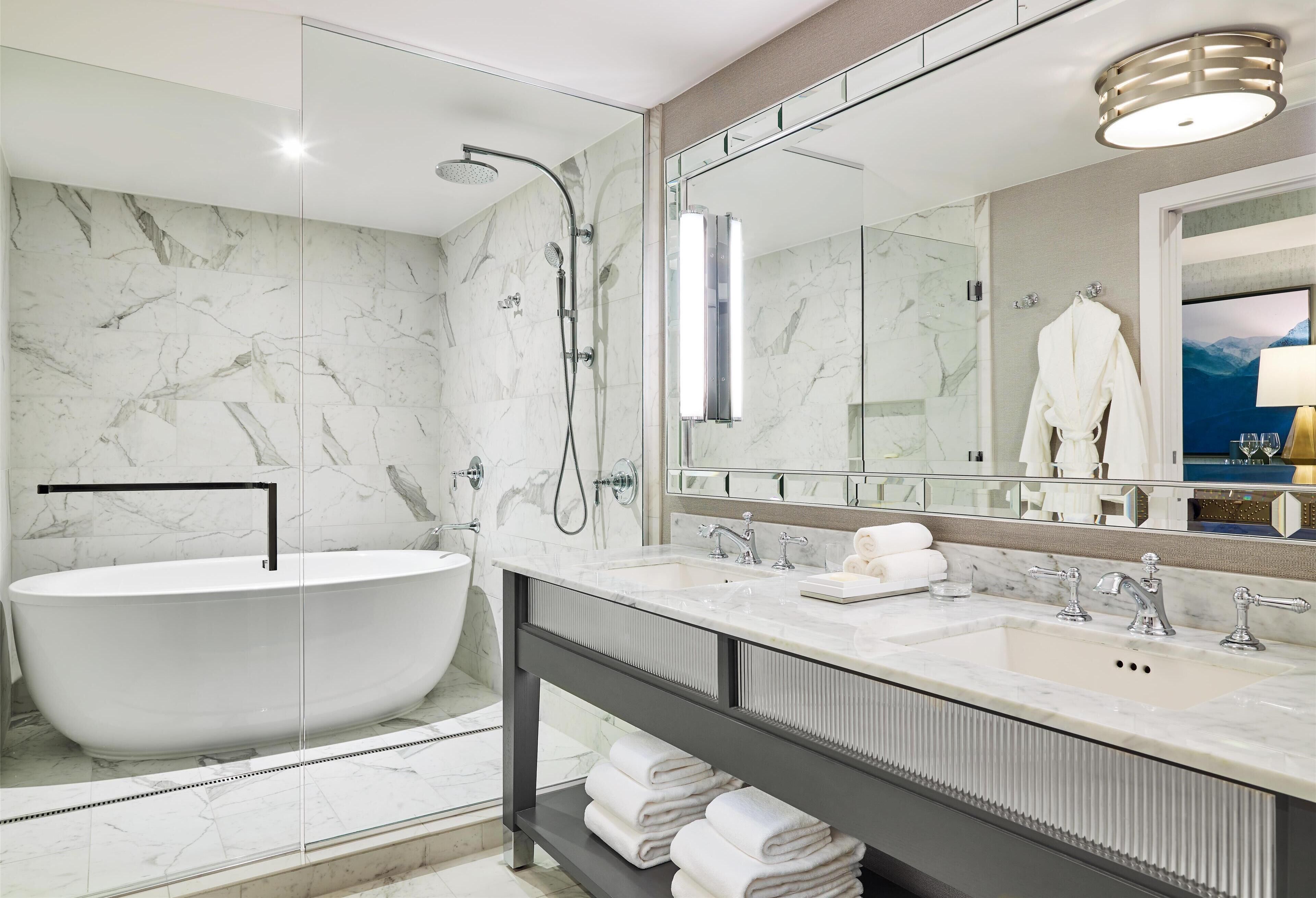 Un baño moderno con una bañera independiente, un espejo grande y un tocador con lavabo y perchero para toallas.