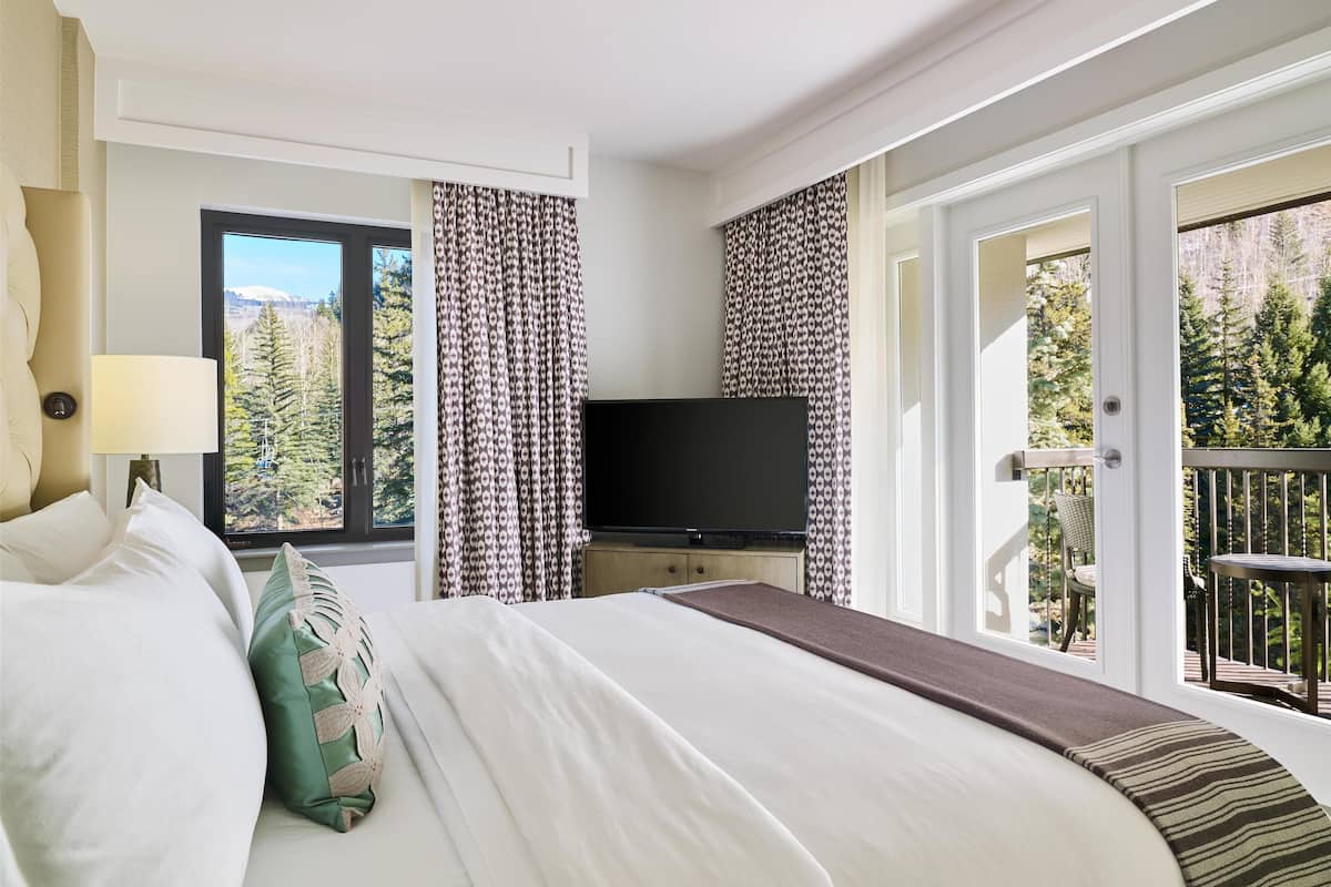 Ein Hotelzimmer mit Bett, Fernseher, einem Fenster mit Vorhängen und einem Balkon mit Geländer.