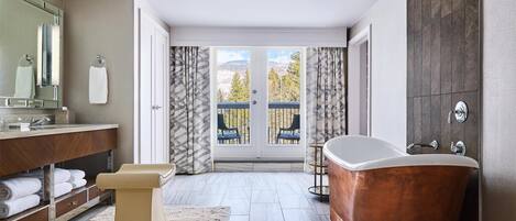 Un baño moderno con una bañera independiente, un espejo grande y vistas a un balcón con mobiliario exterior.
