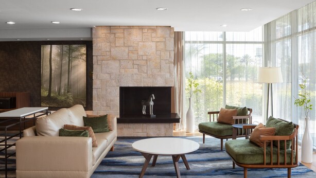 A modern living room with a stone fireplace, comfortable seating, and large windows offering a view of greenery.