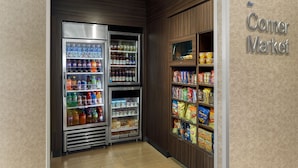 A corner market with refrigerated beverage and snack shelves, wooden paneling, and a sign indicating the location.