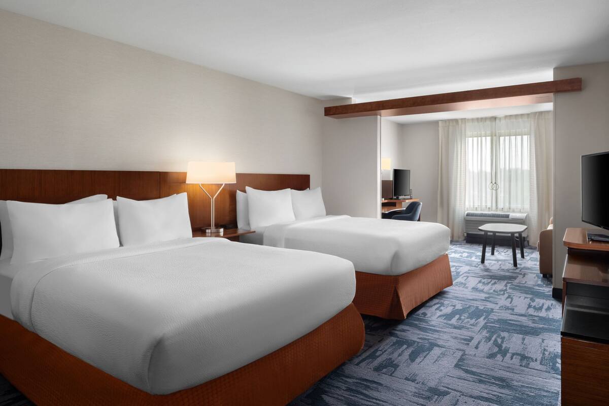 A hotel room with two beds, a desk, a TV, and a window with curtains.
