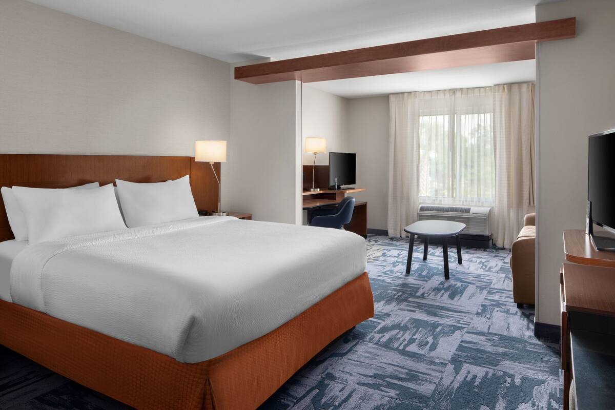 A hotel room with a large bed, a desk with a chair, a television, and a window with curtains.