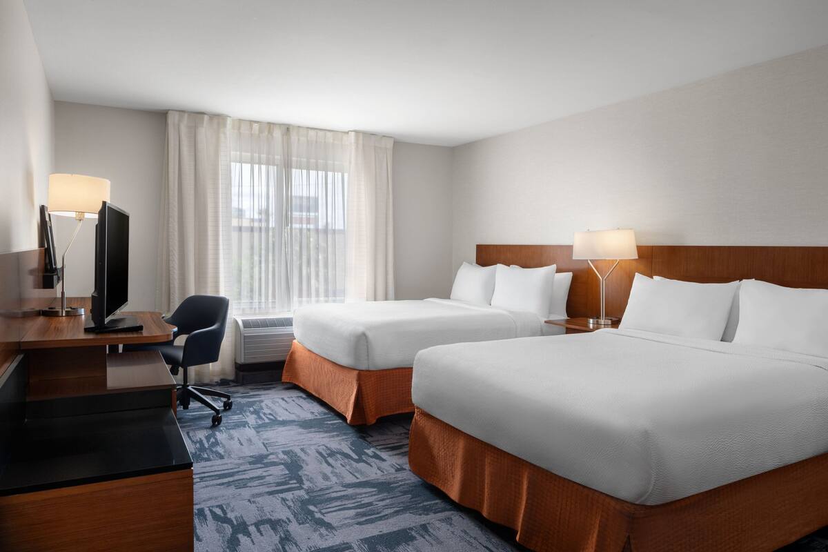 A hotel room with two beds, a desk with a computer, a chair, and two bedside lamps.