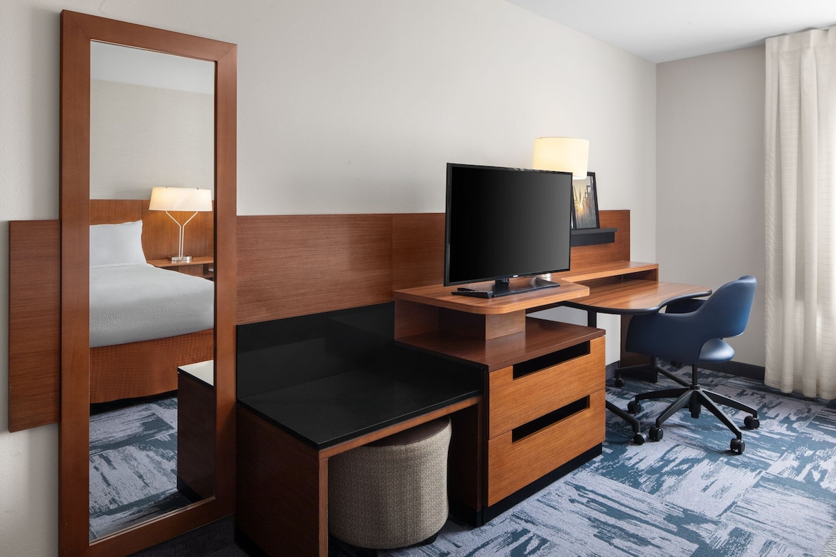 Een hotelkamer met een bed, een bureau met een computer, een stoel, een televisie en een spiegel.